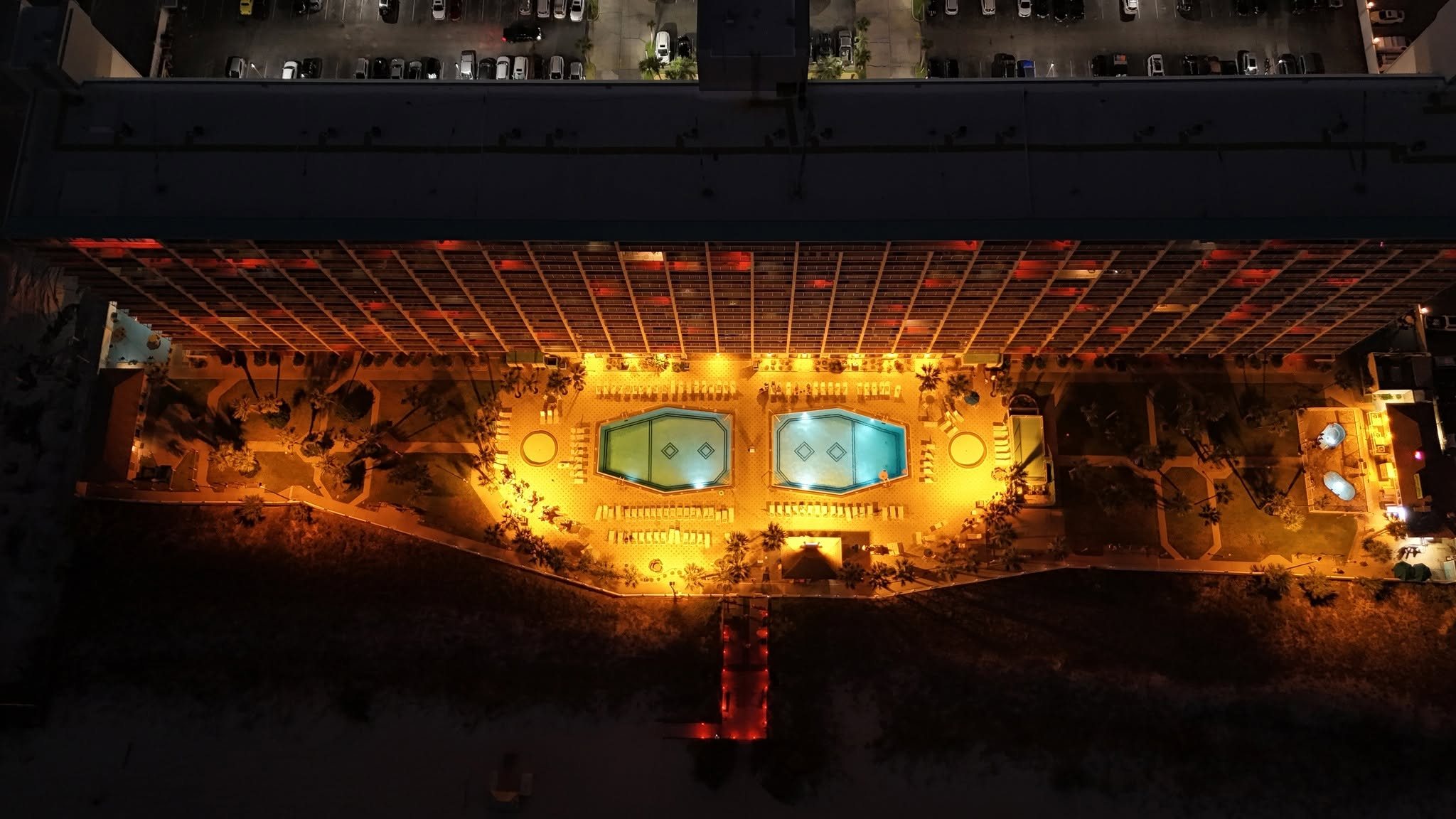 The Summit at night, seen from directly above: the lit pool deck and its two pools between the building and the beach